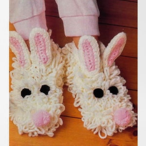 May include: A pair of white crocheted bunny slippers with pink ears and noses. The slippers are fuzzy and have black eyes.
