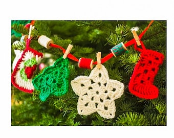May include: A string of crocheted Christmas ornaments hanging on a green Christmas tree. The ornaments are a red stocking, a white star, a green tree, and a red and green stocking.