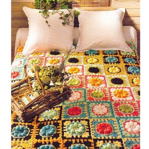 May include: A colorful, handmade crochet blanket with a floral pattern in squares of various colors, including red, yellow, blue, and green. The blanket is on a bed with white pillows and a wooden basket filled with dried flowers.