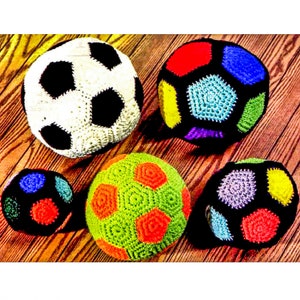 Könnte beinhalten: Fünf gehäkelte Fußbälle in verschiedenen Farben, darunter Schwarz, Weiß, Rot, Blau, Grün, Gelb, Orange und Lila. Die Bälle liegen auf einer Holzoberfläche.