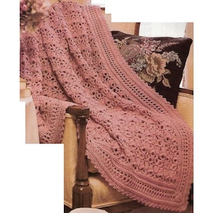 Puede incluir: Una manta de ganchillo rosa con un patrón de encaje, drapeada sobre una silla con una almohada con estampado floral.