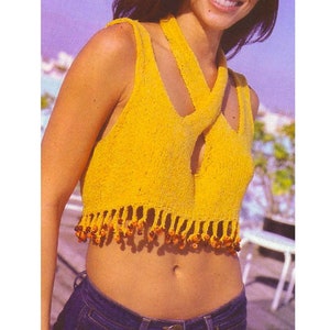 Puede incluir: Un top halter de crochet amarillo con un borde de flecos y cuentas marrones. El top tiene un diseño cruzado en la parte delantera.