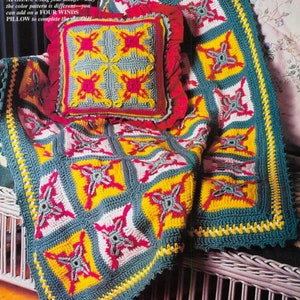 Può includere: Una coperta all'uncinetto colorata con un motivo geometrico in tonalità di verde, giallo, rosa e bianco. La coperta è drappeggiata su una sedia in vimini e presenta un cuscino all'uncinetto abbinato.