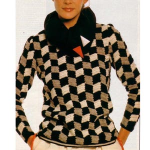 Könnte beinhalten: Ein schwarz-weißer Häkelpullover mit geometrischem Muster. Der Pullover hat einen breiten, schwarzen Kragen und einen roten und weißen Akzent.