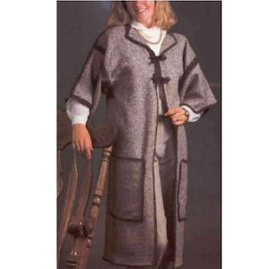May include: A long, gray tweed coat with black trim and large pockets. The coat has a collar and is fastened with two black toggles. The sleeves are three-quarter length. The coat is worn over a white blouse and gray pants.