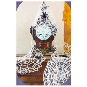 Pu&ograve; includere: Un orologio vintage con quadrante bianco e lancette nere &egrave; ricoperto da ragnatele bianche all'uncinetto. Tre ragni di plastica neri sono posizionati sulle ragnatele.