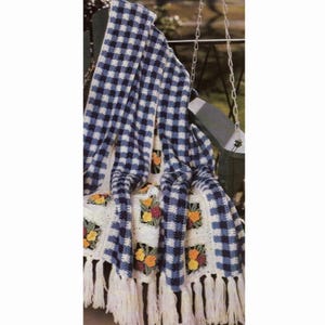 May include: A crocheted throw blanket with a blue and white gingham pattern and floral accents. The blanket has white fringe around the edges.