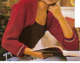 May include: A red crocheted bolero with white and blue trim. The bolero is worn over a black top and blue jeans.