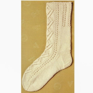 May include: Cream-coloured knitted sock with intricate openwork diamond and vertical stripe patterns. The sock features a ribbed cuff and a detailed design along the leg and foot. The sock is displayed on a yellow background.