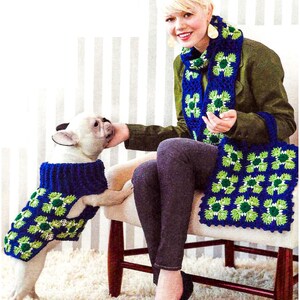 Può includere: Un bulldog francese bianco che indossa un maglione per cani all'uncinetto blu e verde. Una donna è seduta su una sedia con una giacca verde e una sciarpa all'uncinetto blu e verde. La donna tiene una borsa all'uncinetto blu e verde.