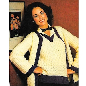 Op de afbeelding: Een gehaakte truiset met een gele cardigan en een paarse trui met V-hals. De cardigan heeft een V-hals en lange mouwen. De trui heeft een V-hals en lange mouwen. Het model draagt een zwarte strik.