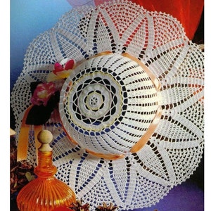 Può includere: Un cappello da sole bianco all'uncinetto con un delicato motivo floreale. Il cappello ha un'ampia tesa e una corona rotonda. È decorato con un nastro bianco e un piccolo fiore.
