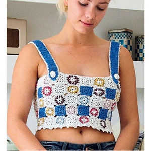May include: A white crochet top with blue straps and a colorful geometric pattern. The top has a square neckline and is cropped.
