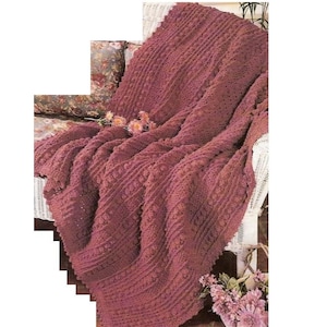 May include: A crocheted throw blanket in a deep burgundy color, draped over a white wicker chair. The blanket has a textured pattern with raised stitches.