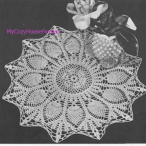 Puede incluir: Un encaje de ganchillo blanco con un diseño circular que presenta un patrón repetitivo de pequeños círculos. El encaje tiene aproximadamente 30 cm de diámetro y se muestra sobre un fondo negro con un jarrón de rosas blancas.