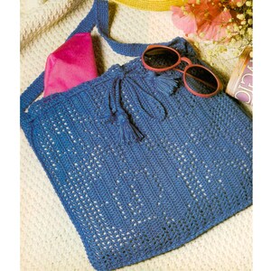 Può includere: Una borsa tote in crochet blu con chiusura a coulisse e nappine. La borsa è realizzata con un delicato motivo a punto aperto e ha una lunga tracolla per essere portata a spalla.