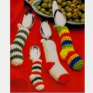 May include: Four silver spoons are wrapped in crocheted Christmas stocking covers. The stockings are red, white, green, and yellow with stripes.