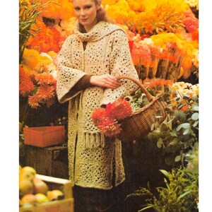 May include: A woman wearing a crocheted beige coat with a fringe hem, standing in front of a flower shop. She is holding a wicker basket filled with flowers.