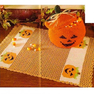 Könnte beinhalten: Ein gehäkelter orangefarbener Kürbis-Korb gefüllt mit Maisbonbons steht auf einem gehäkelten orangefarbenen und weißen Tischläufer mit Kürbis-Design.