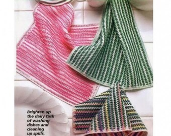 May include: Three crocheted Scrubbie Dishcloths in pink, green, and multicoloured stripes. The text "Scrubbie Dishcloths" is at the top, and the text "Brighten up the daily task of washing dishes and cleaning up spills" is at the bottom.