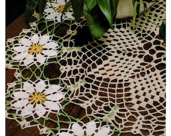 Könnte beinhalten: Ein gehäkelter Tischläufer mit einem weißen und gelben Gänseblümchen-Design. Der Läufer ist aus beigefarbenem und grünem Häkelgarn gefertigt.