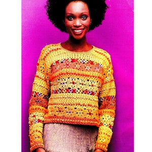 Può includere: Un maglione all'uncinetto nei toni del giallo, arancione e marrone. Il maglione presenta uno scollo tondo e maniche lunghe. Il design include strisce orizzontali e motivi traforati con accenti rossi e viola. Il maglione è indossato da una persona con i capelli scuri.
