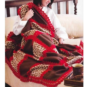 May include: A brown fleece blanket with a leopard print pattern and red crocheted trim. The blanket is folded and draped over a couch.