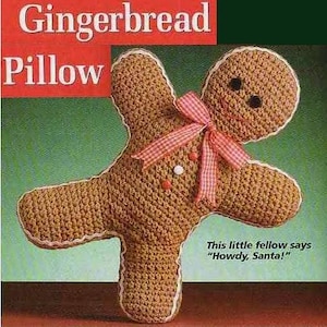 May include: A crocheted gingerbread man pillow with a red and white ribbon bow, white trim, and black button eyes. The text "Gingerbread Pillow" is in a red box. The pillow says, "Howdy, Santa!"