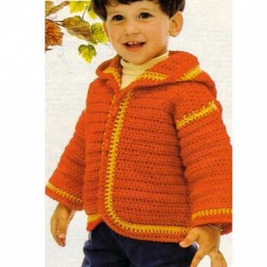 Peut inclure: Une veste à capuche orange crochetée avec une bordure jaune, portée par un enfant. La veste a une fermeture à boutons et des détails jaunes sur la capuche et les bords. Vêtement fait main et confortable.