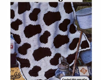 May include: A white and dark brown crocheted blanket with a cowhide pattern. The blanket is displayed over a wooden fence. The text "Holstein Afghan" is at the top. The text "Crache? this one-of-a-kind cover for the country-loving person on your gift list" is at the bottom.