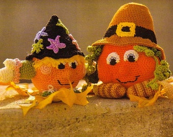 Könnte beinhalten: Zwei gehäkelte Kürbisfiguren, eine als Hexe mit einem schwarzen Hut und die andere als Pilger mit einem braunen Hut, sitzen auf einer braunen Oberfläche mit Herbstblättern.
