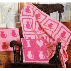 May include: A pink crocheted blanket with a cat design, two pink crocheted pillows with cat designs, and one pink crocheted pillow with the text "I love" and a heart design.