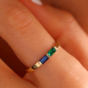 May include: A gold ring featuring three rectangular gemstones in blue, green, and blue. The ring has a slim band and a minimalist design. The gemstones are set in a row, creating a simple and elegant look. The ring is a piece of jewellery.