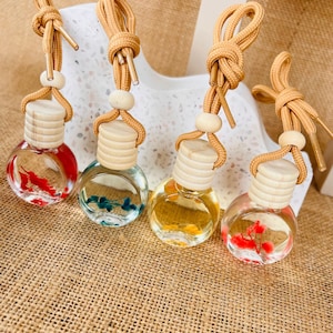 May include: Four small glass bottles with cork stoppers and string hangers. The bottles are filled with a clear liquid and contain small dried flowers. The bottles are red, blue, yellow, and red.