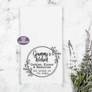 May include: White kitchen towel with a black circle design that says "Grammy's kitchen Cookies, Kisses & Memories are always on the menu."