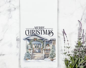May include: A white kitchen towel with a watercolor illustration of a house with a porch and a wreath on the door. The text "Merry Christmas" is printed above the house.