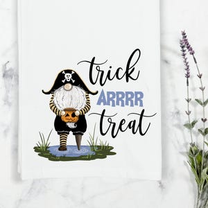 May include: A white kitchen towel with a black and white illustration of a pirate gnome holding a jack-o-lantern. The text "trick arrrr treat" is written in black cursive.