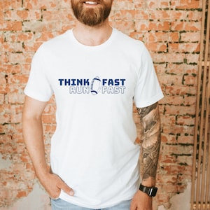 May include: White t-shirt with a blue graphic of a football and the text "Think Fast Run Fast".