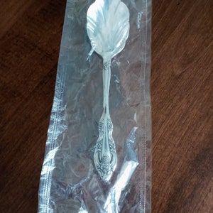 May include: A silver sugar spoon with an ornate design on the handle. The spoon is packaged in a clear plastic bag.