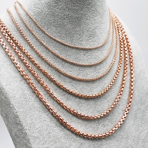 May include: A display of six rose gold-colored chain necklaces of varying thicknesses. The necklaces are arranged on a gray mannequin bust, showcasing their different sizes and styles. The chains have a rounded, box-link design.