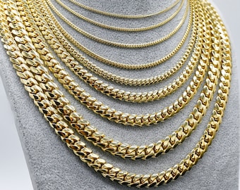 May include: A set of gold chain necklaces of varying widths and lengths. The chains are layered on a gray mannequin.