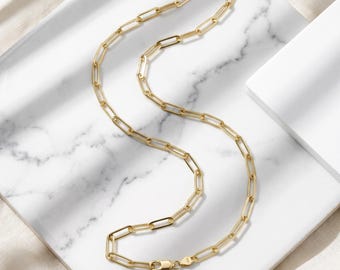 May include: A gold-toned paperclip chain necklace featuring elongated rectangular links with a polished finish. The necklace includes a secure lobster claw clasp mechanism at the end, showcasing a consistent metallic yellow hue throughout the entire piece.