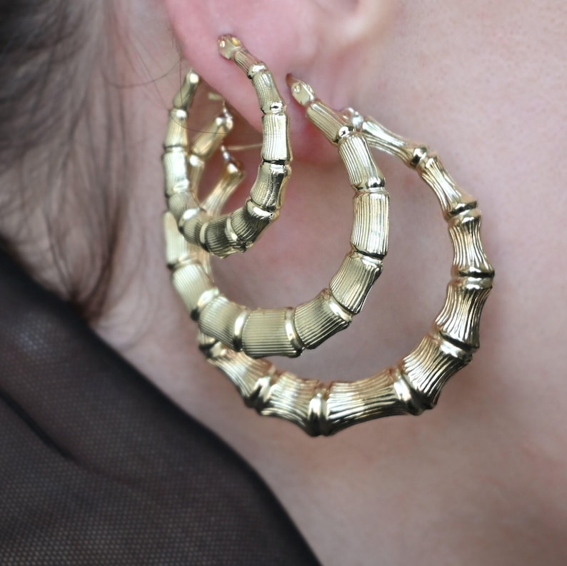 A woman's ear with two gold bamboo-style hoop earrings, one large and one smaller, nested together.