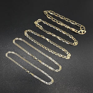 Five gold mariner chain bracelets arranged in a parallel diagonal line on a black textured surface.
