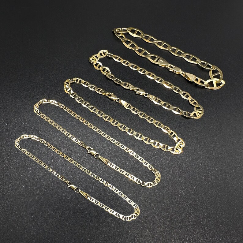 Five gold mariner chain bracelets arranged in a parallel diagonal line on a black textured surface.