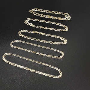 Five gold mariner chain bracelets of varying thickness laid out diagonally on a black surface.