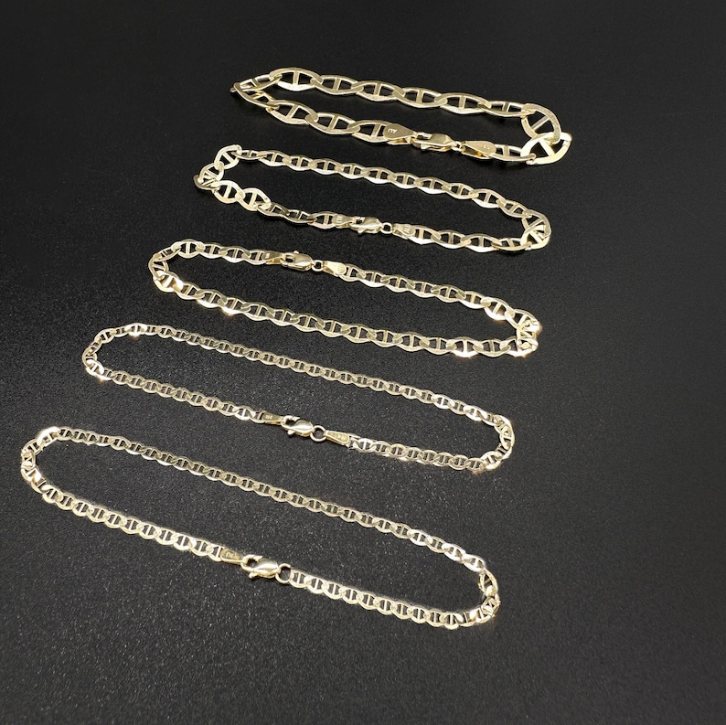 Five gold mariner chain bracelets of varying thickness laid out diagonally on a black surface.