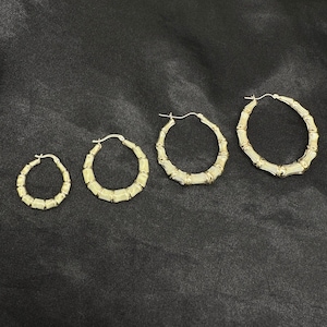 Four gold bamboo-style hoop earrings of increasing size are laid out in a row on a black fabric surface.
