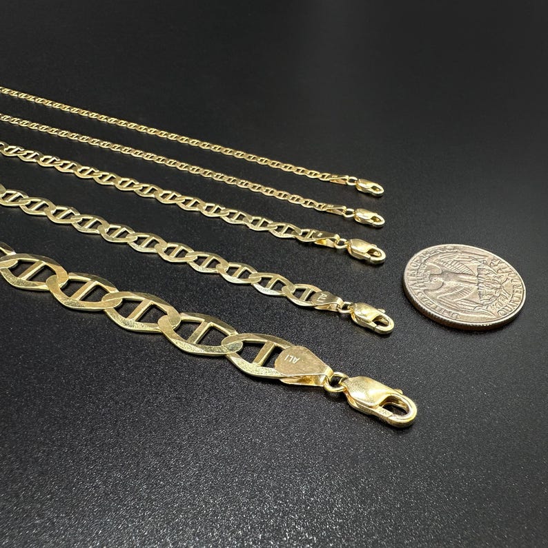 Four gold mariner chains of increasing thickness laid horizontally next to a US quarter coin for scale.