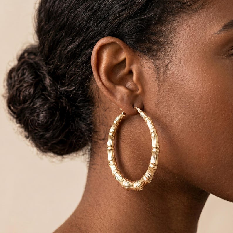 A woman's ear with a single large, gold, bamboo-style hoop earring, showing the earring's textured surface and a secure clasp.